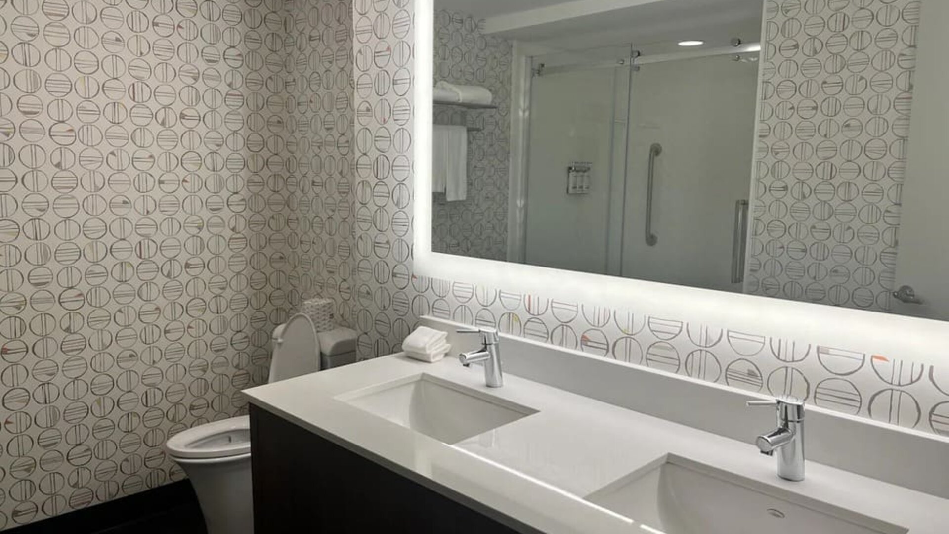 Modern hotel bathroom featuring a double vanity, illuminated mirror and an accessible walk-in shower at Holiday Inn Toronto Airport East.