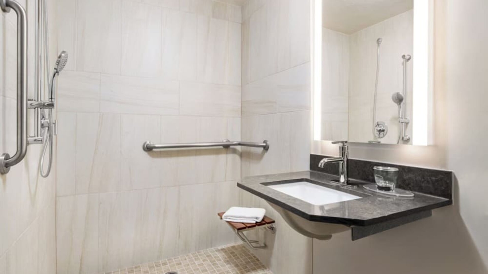 Accessible walk-in bathroom featuring grab bars, a handheld shower and a modern vanity designed for added convenience at Candlewood Suites Boise.