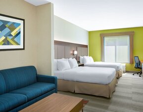 Guest room featuring two beds, a sofa, a work desk and modern décor designed for comfort at Holiday Inn Express & Suites Ontario.