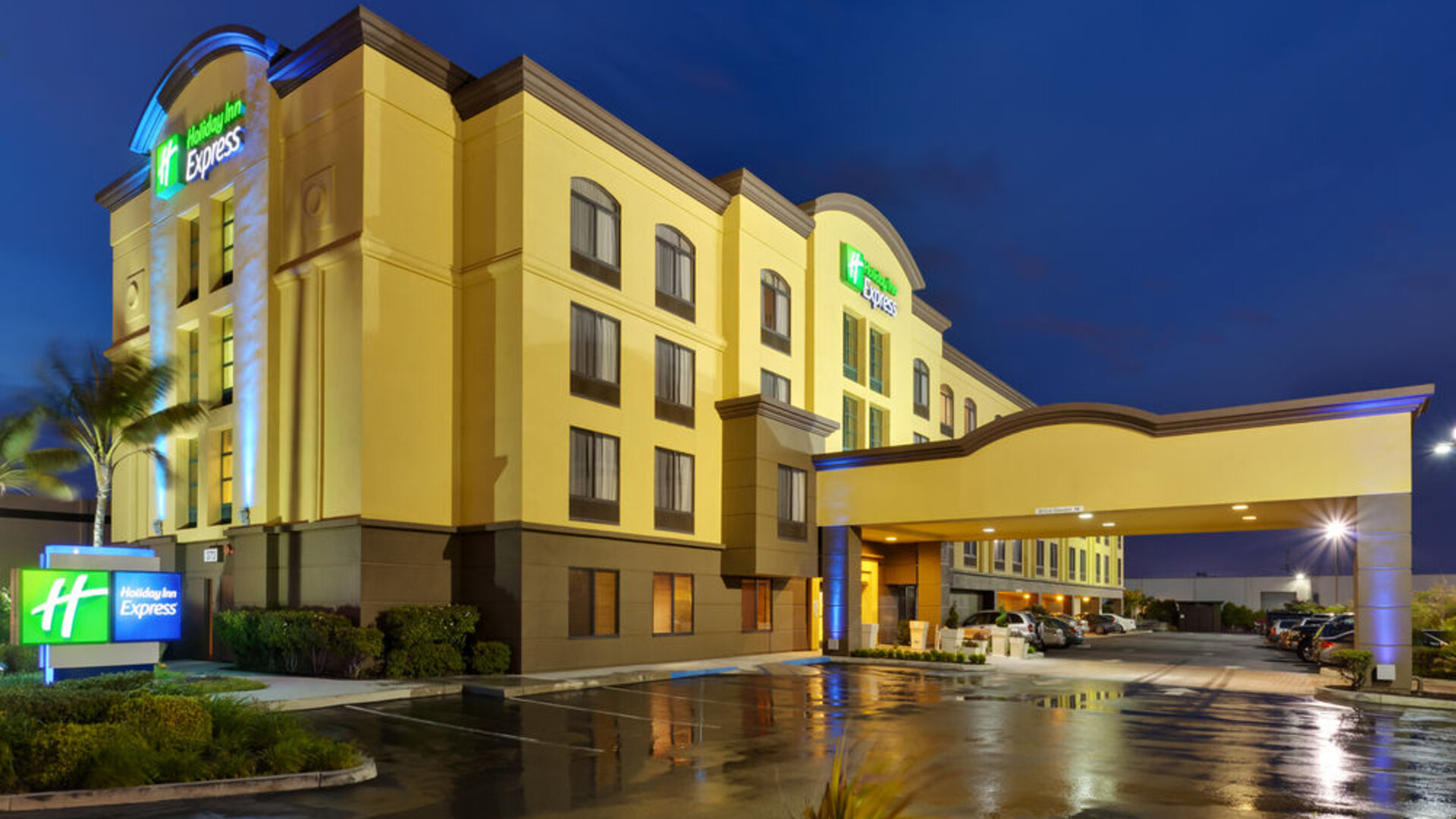 Evening exterior view featuring illuminated architecture, a covered porte cochère and a welcoming entrance at Holiday Inn Express SFO Airport North.
