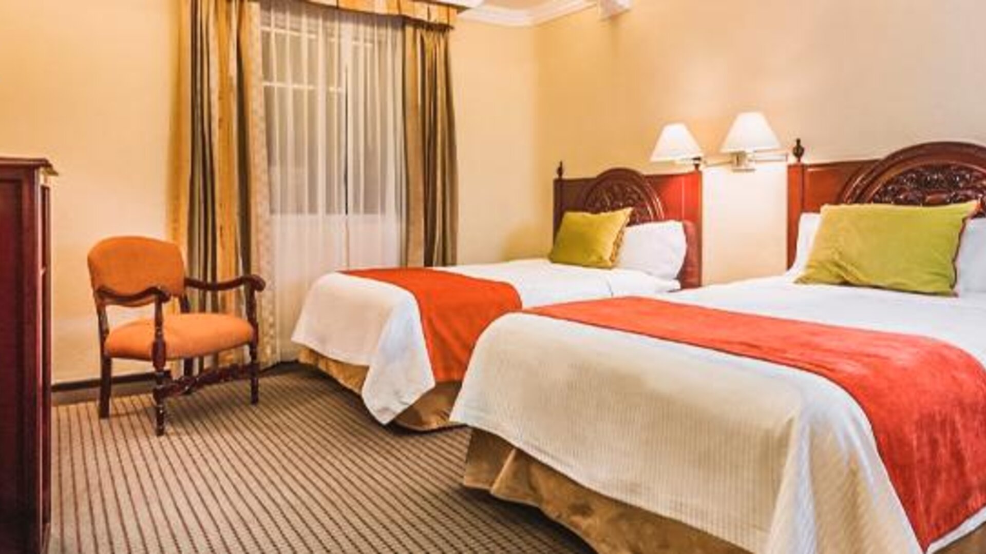 Guest room with two beds featuring carved wood furnishings, accent pillows, bedside lighting, and traditional décor at Hotel Geneve.