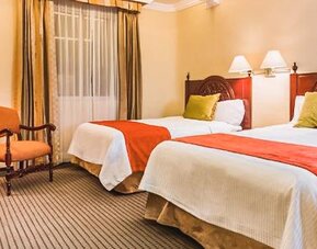 Guest room with two beds featuring carved wood furnishings, accent pillows, bedside lighting, and traditional décor at Hotel Geneve.