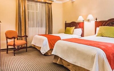 Guest room with two beds featuring carved wood furnishings, accent pillows, bedside lighting, and traditional décor at Hotel Geneve.
