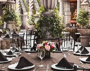 Dining area featuring round tables, formal place settings, decorative columns, plants, and an open atrium design at Hotel Geneve.