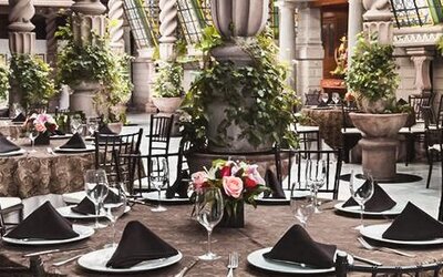 Dining area featuring round tables, formal place settings, decorative columns, plants, and an open atrium design at Hotel Geneve.