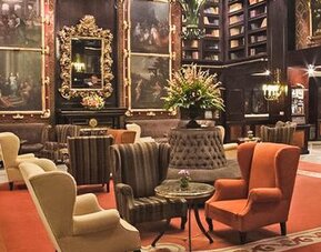 Grand lounge featuring dark wood décor, artwork, floor-to-ceiling bookshelves, and multiple seating areas at Hotel Geneve.