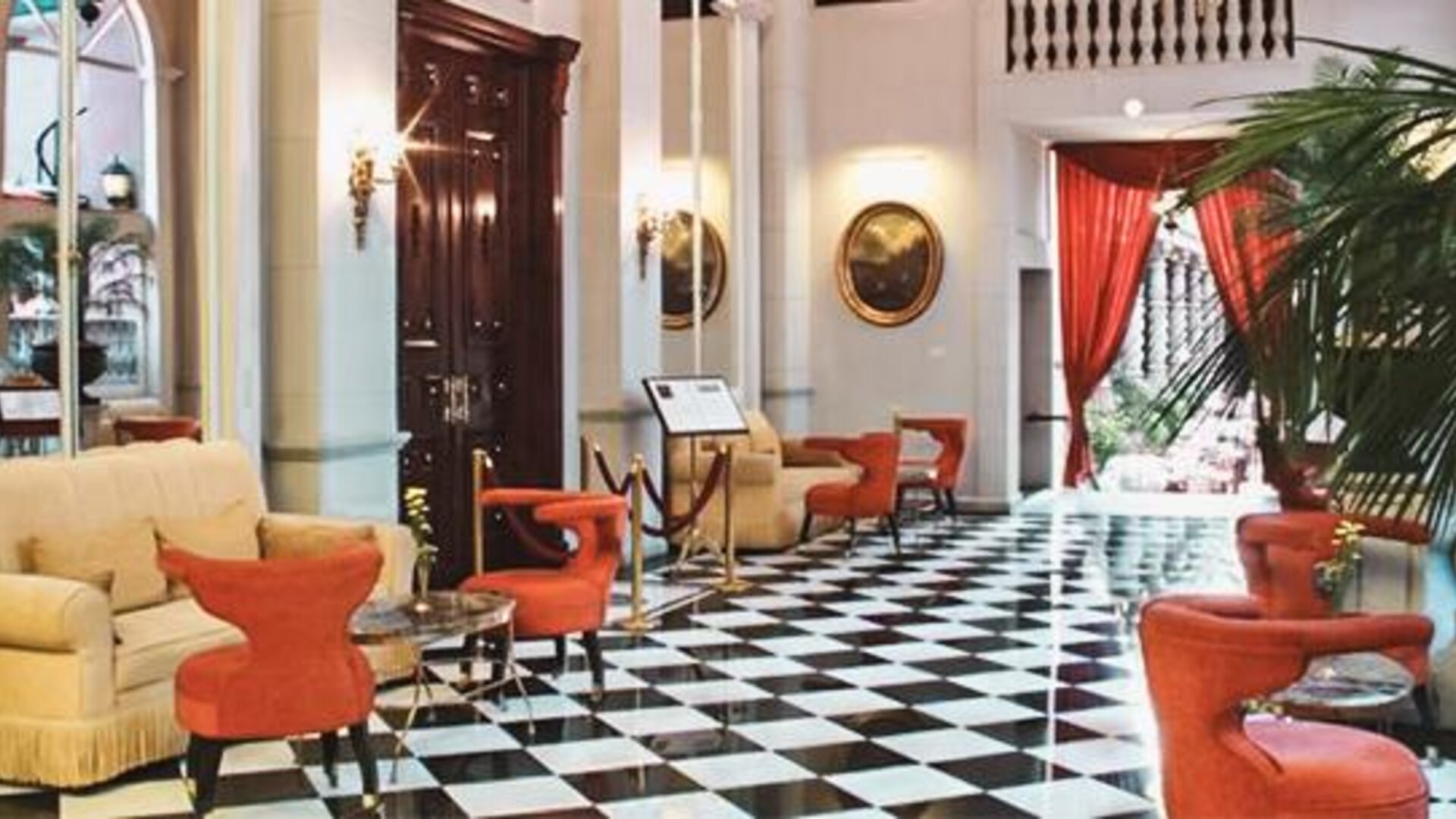 Elegant lobby featuring black-and-white tiled flooring, high ceilings, comfortable seating, and dramatic red drapery at Hotel Geneve.