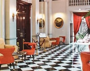 Elegant lobby featuring black-and-white tiled flooring, high ceilings, comfortable seating, and dramatic red drapery at Hotel Geneve.