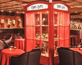 Piano bar featuring intimate table seating, decorative display cabinets, a fully stocked bar, and warm ambient lighting at Hotel Geneve.