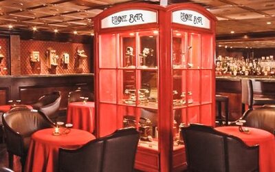 Piano bar featuring intimate table seating, decorative display cabinets, a fully stocked bar, and warm ambient lighting at Hotel Geneve.