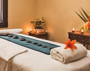 Spa treatment room featuring a massage table, decorative candles, floral arrangements, and a relaxing atmosphere at Hotel Geneve.