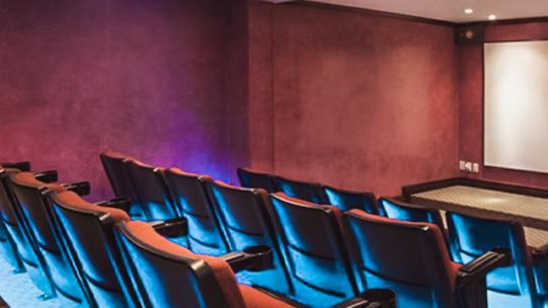 Private theater with tiered seating, blue accent lighting, and a large projection screen at Hotel Geneve.