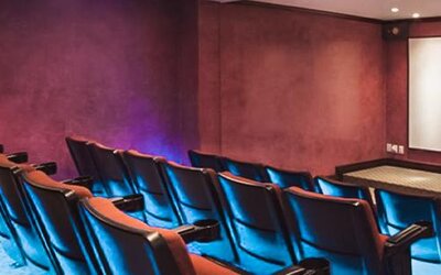 Private theater with tiered seating, blue accent lighting, and a large projection screen at Hotel Geneve.
