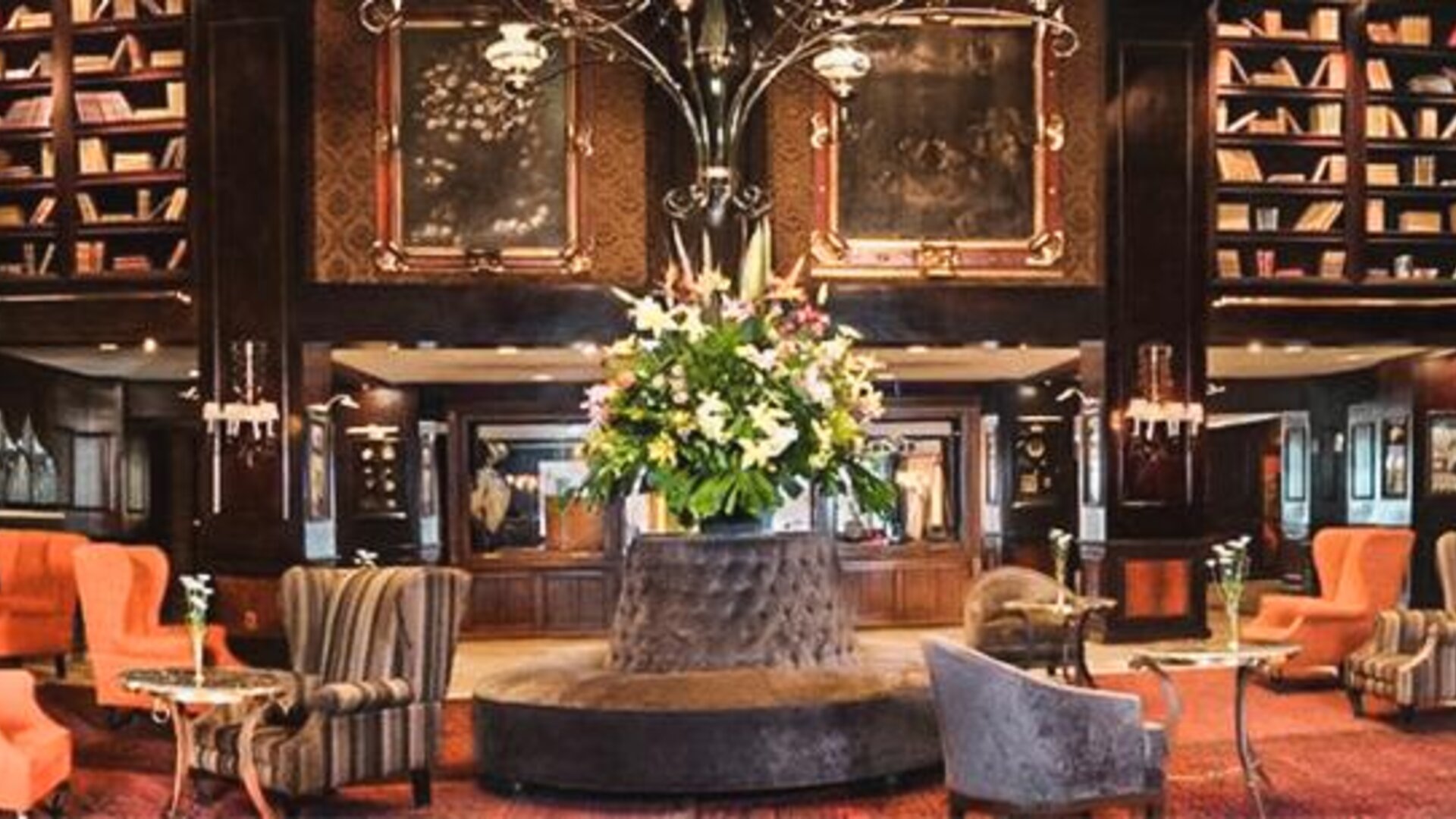 Spacious lobby featuring a central floral arrangement, floor-to-ceiling bookshelves, chandeliers, and multiple seating areas at Hotel Geneve.