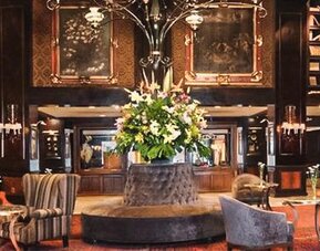 Spacious lobby featuring a central floral arrangement, floor-to-ceiling bookshelves, chandeliers, and multiple seating areas at Hotel Geneve.