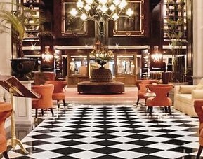 Elegant lobby with black-and-white tiled flooring, chandeliers, plush seating, and a grand entrance at Hotel Geneve.