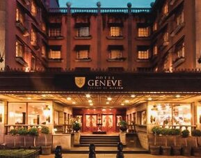 Exterior view of the grand entrance featuring the illuminated marquee, landscaped walkways, and traditional architectural details at Hotel Geneve.
