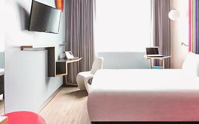 Guest room featuring a bed, workspace, wall-mounted television, contemporary furnishings, and colorful accent walls at Ibis Styles Mexico Reforma.
