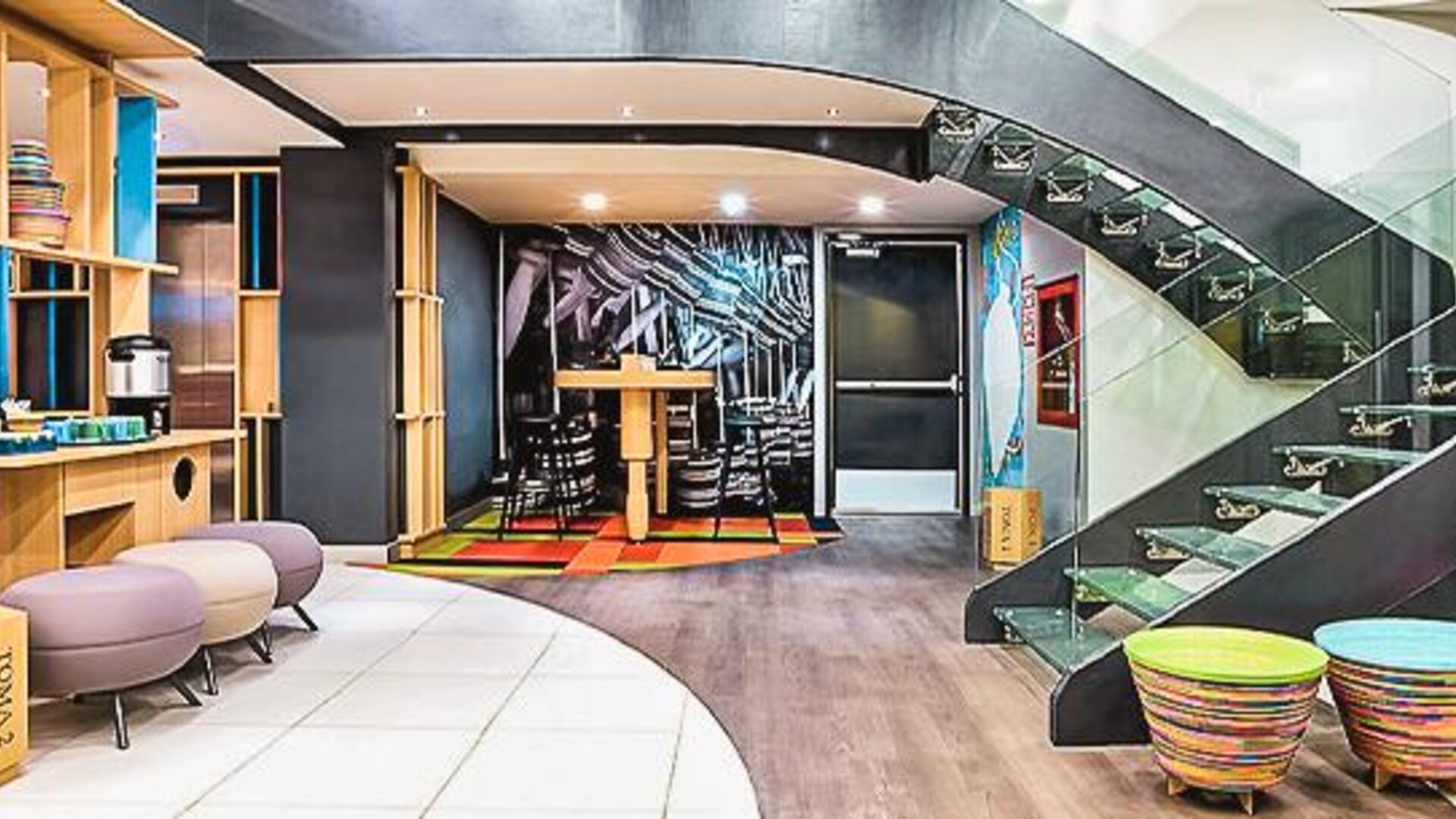 Modern lobby with contemporary seating, open shelving, colorful décor, and a glass staircase at Ibis Styles Mexico Reforma.
