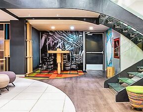 Modern lobby with contemporary seating, open shelving, colorful décor, and a glass staircase at Ibis Styles Mexico Reforma.