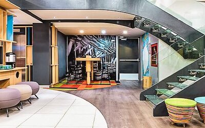 Modern lobby with contemporary seating, open shelving, colorful décor, and a glass staircase at Ibis Styles Mexico Reforma.