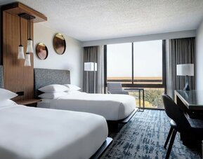 Guest room featuring two beds, floor-to-ceiling windows, a dedicated workspace, and contemporary furnishings at Houston Marriott South at Hobby Airport.