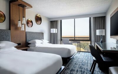 Guest room featuring two beds, floor-to-ceiling windows, a dedicated workspace, and contemporary furnishings at Houston Marriott South at Hobby Airport.