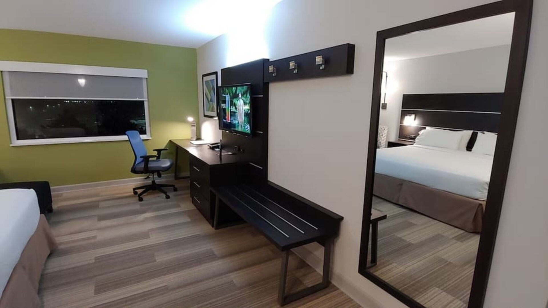 In-room workspace featuring a large desk, flat-screen television, luggage bench, and full-length mirror at Holiday Inn Express Rolling Meadows-Schaumburg.