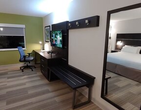 In-room workspace featuring a large desk, flat-screen television, luggage bench, and full-length mirror at Holiday Inn Express Rolling Meadows-Schaumburg.
