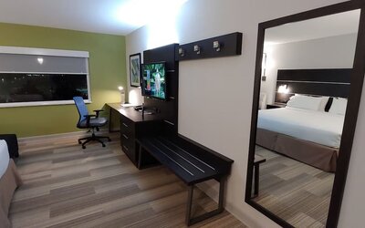 In-room workspace featuring a large desk, flat-screen television, luggage bench, and full-length mirror at Holiday Inn Express Rolling Meadows-Schaumburg.