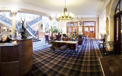 Grand hotel lobby featuring tartan carpeting, elegant seating, a sweeping staircase, and traditional Scottish décor at The Royal Highland Hotel.