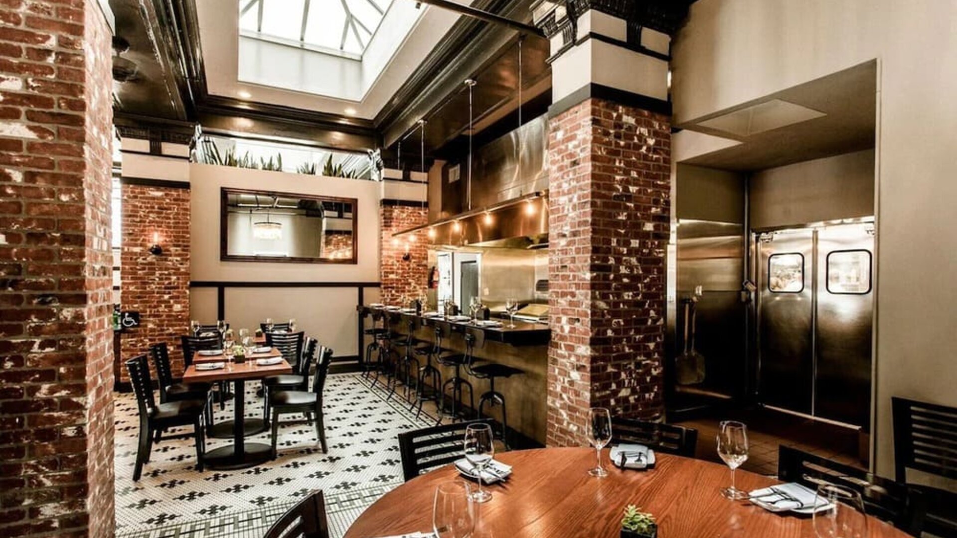 Dining area featuring an open kitchen, exposed brick accents, skylights, and contemporary seating at The Mosser Hotel.