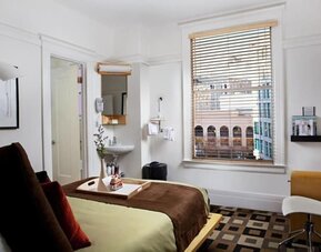Guest room featuring large windows with city views, a writing desk, an open vanity area, and contemporary furnishings at The Mosser Hotel.