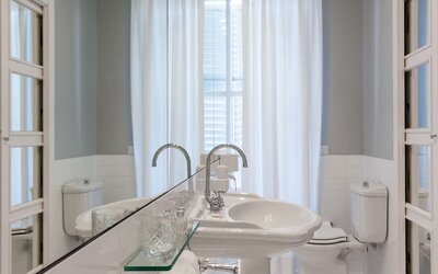 Bathroom featuring a pedestal sink, oversized mirror, bright natural light, and classic European design at Cellai Boutique Hotel.