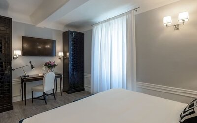 In-room workspace featuring a writing desk, upholstered chair, wall-mounted television, and contemporary furnishings at Cellai Boutique Hotel.