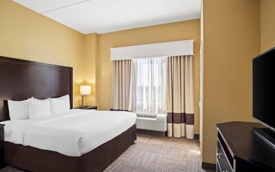 Guest room with a king-size bed, work desk, flat-screen television, and large window with blackout curtains at Comfort Suites Frisco.