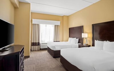 Guest room with two queen beds, a work desk, dresser, and large window providing natural light at Comfort Suites Frisco.