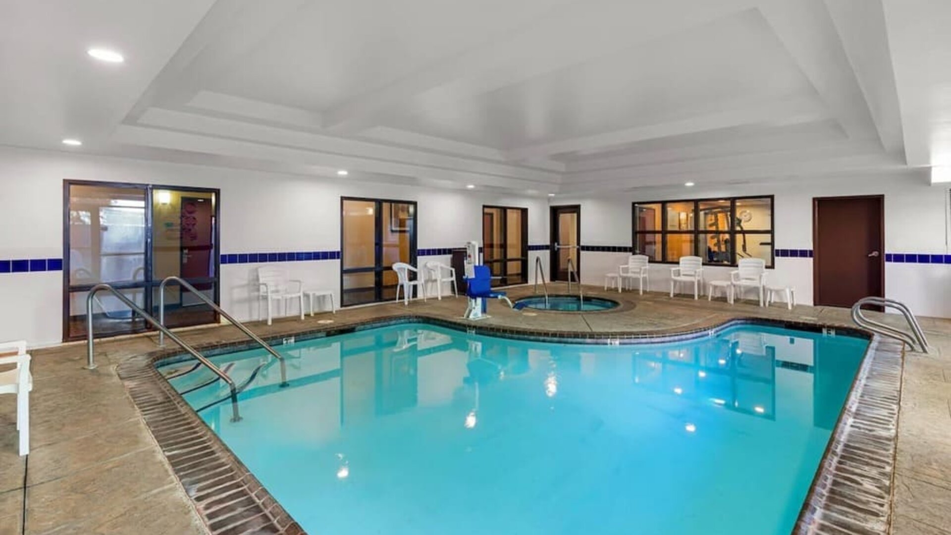 Indoor swimming pool with a hot tub, poolside seating, and accessible pool lift at Comfort Suites Vacaville-Napa Valley Area.