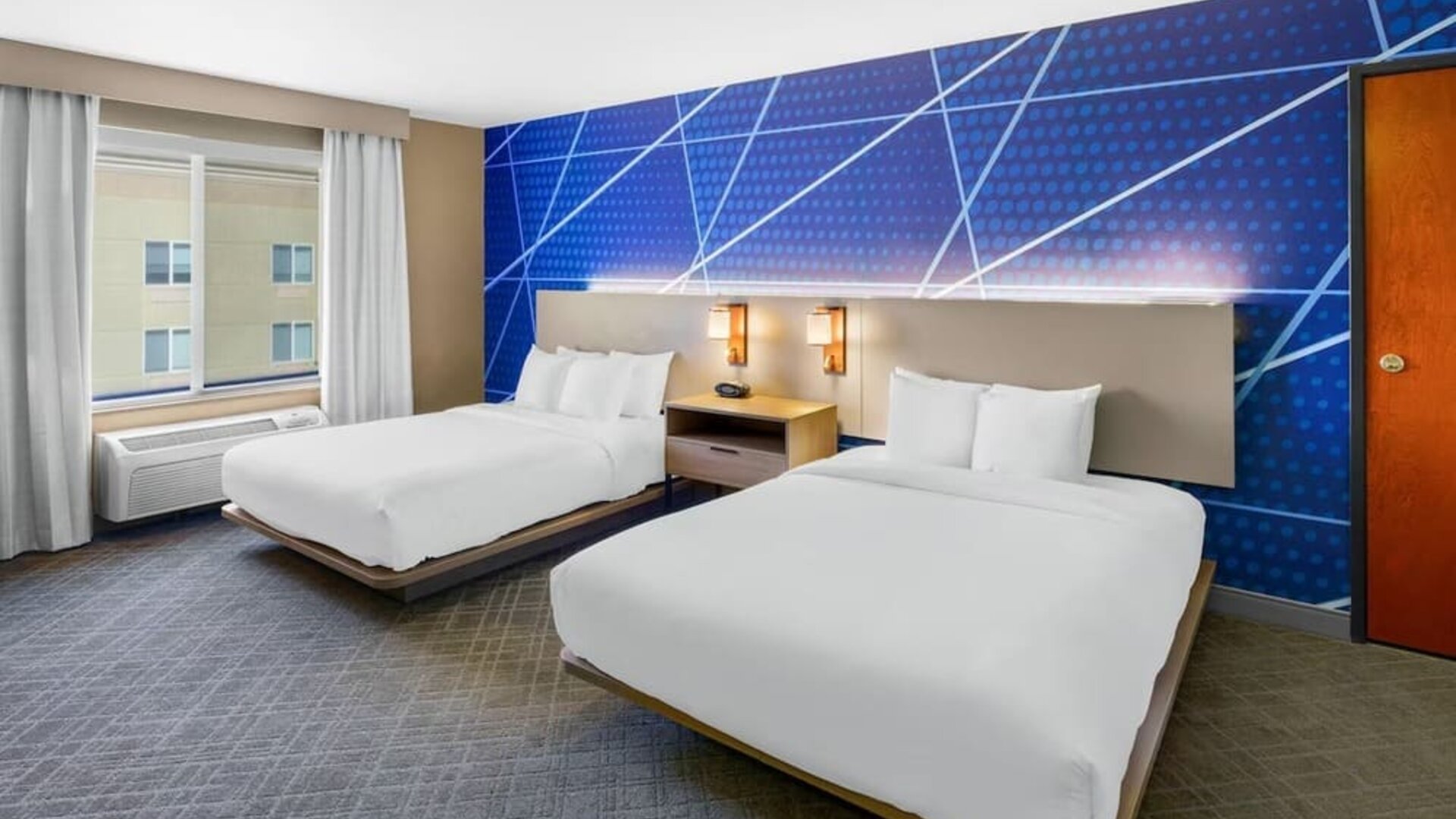 Guest room featuring two queen beds, modern blue accent décor, bedside lighting, and a large window at Comfort Suites Vacaville-Napa Valley Area.