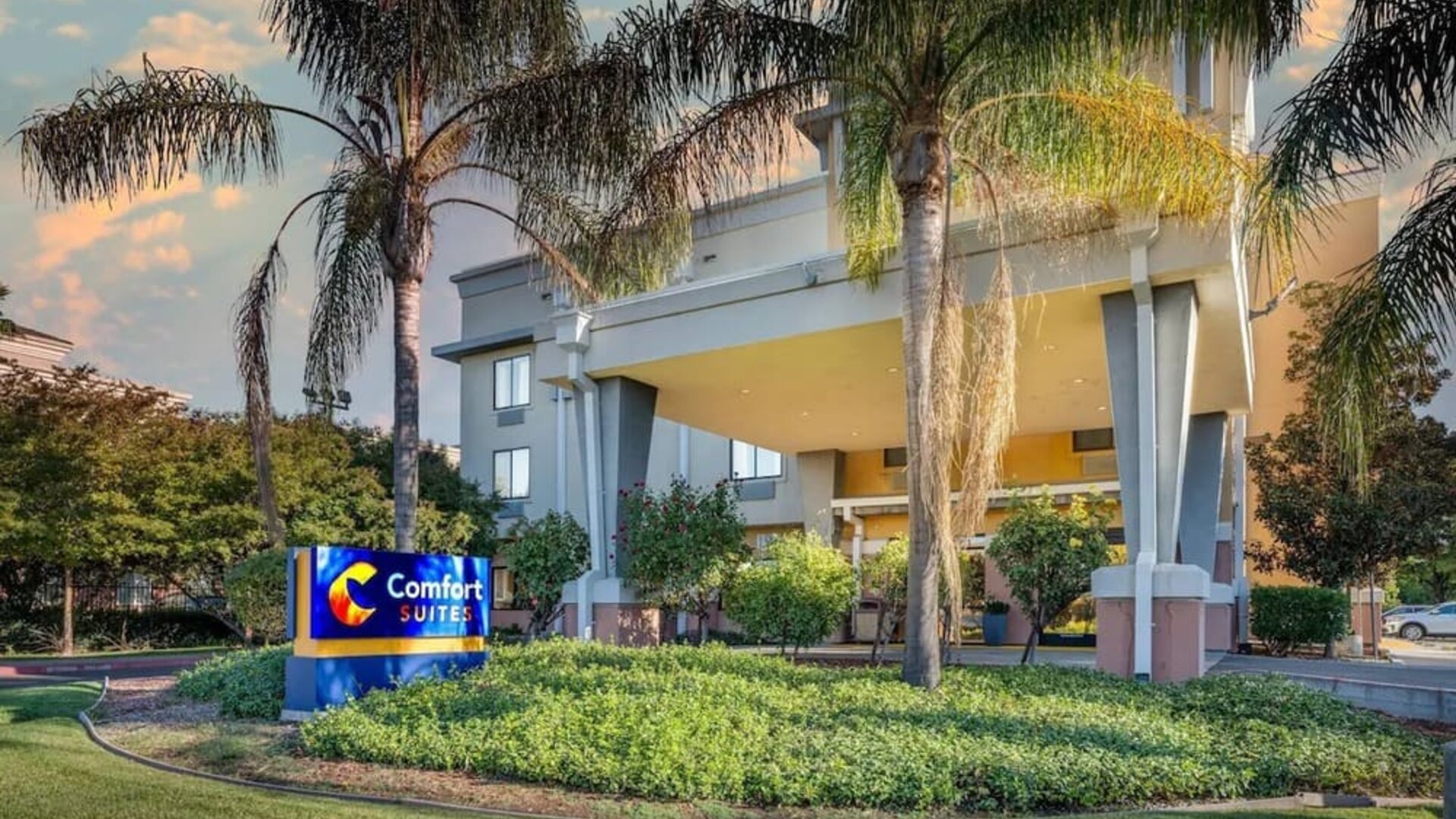 Exterior view of the hotel entrance surrounded by palm trees and landscaped grounds at Comfort Suites Vacaville-Napa Valley Area.
