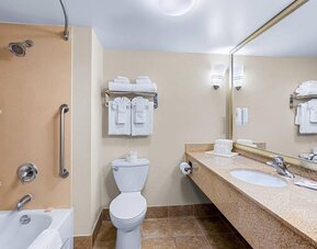 Guest bathroom featuring a bathtub and shower combination, granite vanity, large mirror, and fresh towels at Comfort Suites Vacaville-Napa Valley Area.