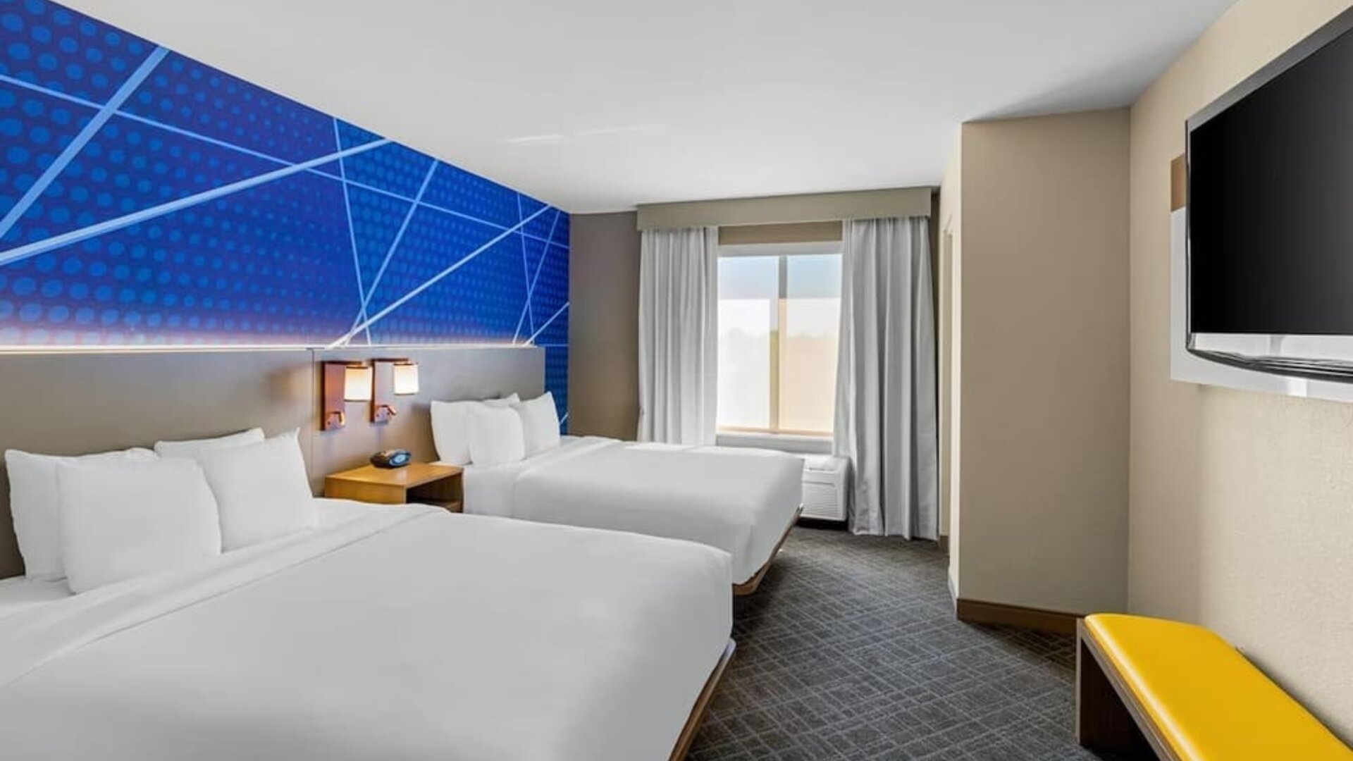 Guest room with two queen beds, modern blue accent décor, a flat-screen television, and natural light at Comfort Suites Vacaville-Napa Valley Area.