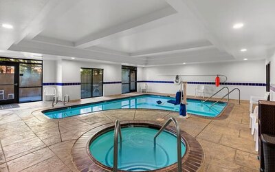 Indoor pool and hot tub area with poolside seating, handrails, and an accessible pool lift at Comfort Suites Vacaville-Napa Valley Area.