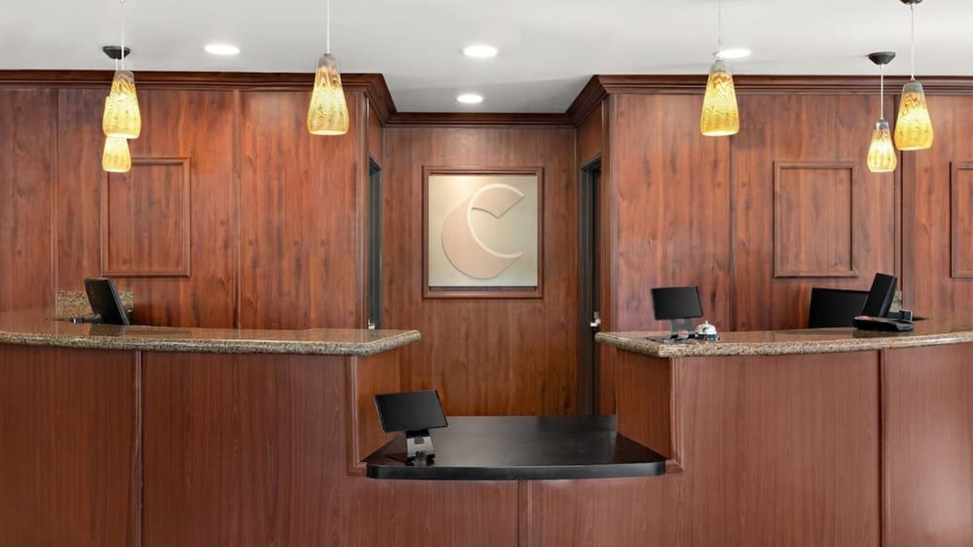 Front desk and reception area featuring granite counters, warm wood finishes, and pendant lighting at Comfort Suites Vacaville-Napa Valley Area.