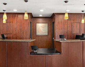 Front desk and reception area featuring granite counters, warm wood finishes, and pendant lighting at Comfort Suites Vacaville-Napa Valley Area.