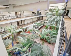 Interior atrium featuring lush tropical plants, open corridors, and decorative railings at Coratel Plus Suites Wichita West Airport.