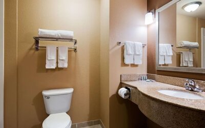 Guest bathroom featuring a granite vanity, large mirror, fresh towels, and shower area at Best Western Granbury Inn & Suites.