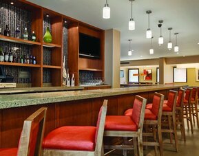 Contemporary hotel bar featuring countertop seating, pendant lighting, beverage displays, and a flat-screen television at Hyatt Place San Jose Downtown.