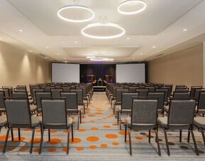 Spacious meeting facility arranged theatre-style with rows of chairs, presentation screens, and a stage area at Hyatt Place San Jose Downtown.