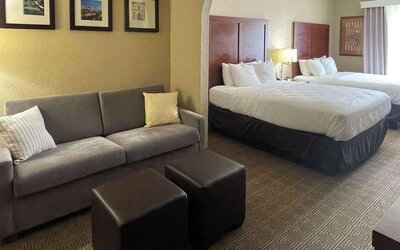 Spacious guest suite with two beds, sofa, ottomans, bedside lighting, and separate seating area at Comfort Suites San Antonio SeaWorld - Lackland AFB.